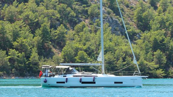 Die Segelyacht Sam's Wave segelt auf dem Wasser vor einer grünen Kulisse, die Ruhe ausstrahlt.