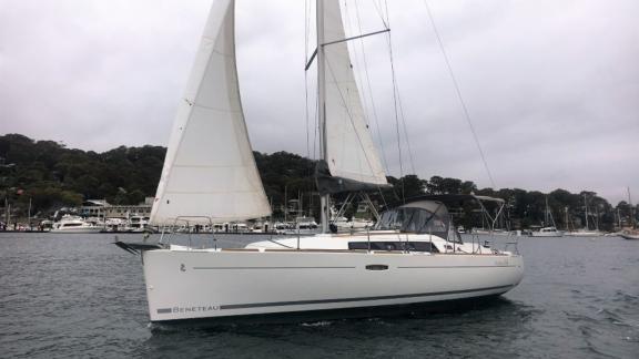 The sailing yacht Çakıl glides through the harbor, with yachts and trees visible in the background.