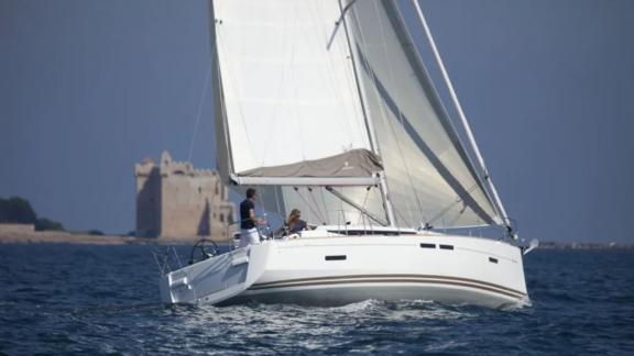 The Mercann sailing yacht cruises on the sea with a castle visible in the background.