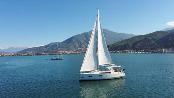 Die Segelyacht Rosa Bella segelt friedlich auf dem Wasser mit einer Bergkulisse im Hintergrund.