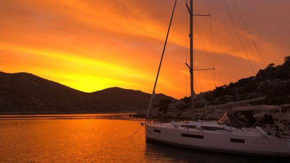 Die Segelyacht Yakamozi liegt bei Sonnenuntergang in einer ruhigen Bucht vor Anker.