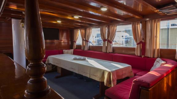 Geräumiger und eleganter Salon mit roten Polstern und großen Fenstern auf der Gulet Erşen 1 im Hafen von Bodrum.