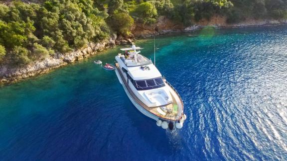 Die Motoryacht Samocla liegt vor Anker in Küstennähe, umgeben von grünen Bäumen und blauem Wasser.
