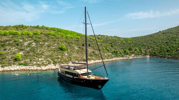 The luxury yacht Santa Clara anchored in a tranquil, picturesque bay with green hills.