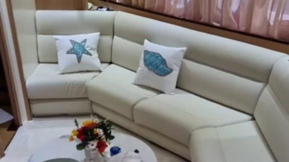 Im Inneren der Motoryacht Aron 26 befindet sich ein heller Ecksofa mit maritimen Kissen und ein kleiner Tisch mit Blumen