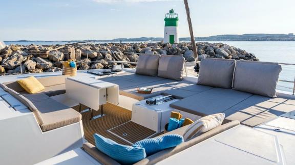 The stylish seating area of the Bali 5.4 catamaran offers a stunning view of a lighthouse along the Italian coast.