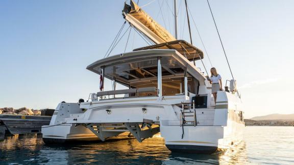 The Bali 5.4 catamaran is anchored in an Italian harbor, illuminated by the warm glow of the setting sun.