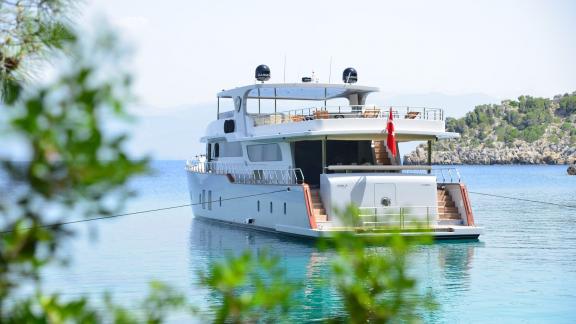 The Simay F yacht is anchored in a serene bay surrounded by trees, offering a relaxing view.