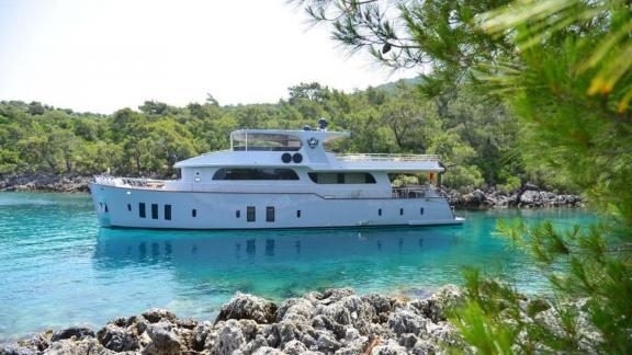 The Simay F yacht is anchored in a serene bay surrounded by trees, offering a relaxing view.