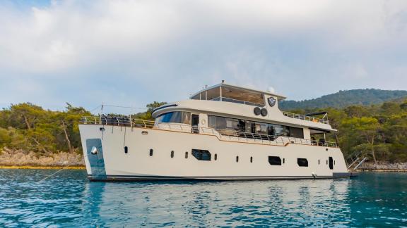 Yacht Simay M vor Anker in einer ruhigen Bucht, umgeben von Grün und blauem Wasser.