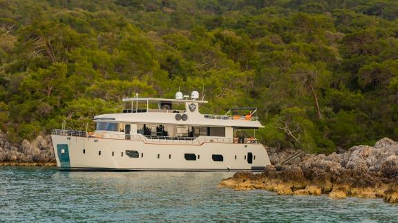 Die Yacht Simay M vor Anker in einer grünen, bewaldeten Gegend, umgeben von natürlicher Landschaft.