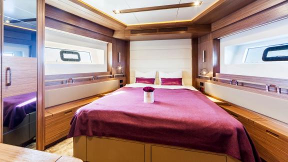 Two side windows and a cozy bed with purple cover on Sirena 64.