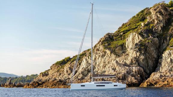 Segelyacht Sirius II liegt vor Anker an einer felsigen Küste in ruhigem Wasser.