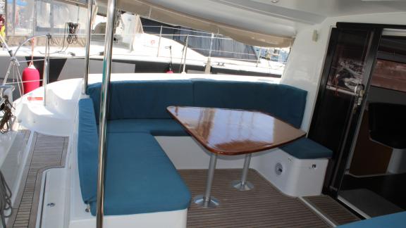 Blue U-shaped seating area with a shiny wooden table on Catamaran Ayda1.