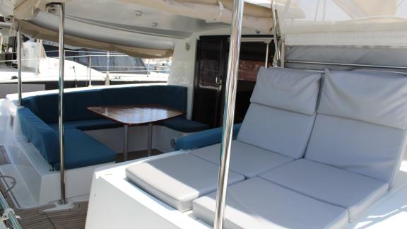 Blue seating area with wooden table and grey sun loungers on Catamaran Ayda1.