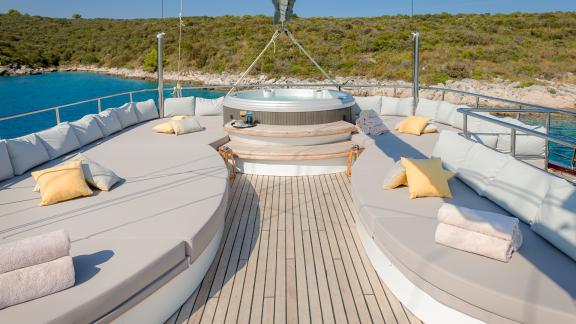 Роскошное джакузи и просторная зона для загара с подушками на палубе Lady Gita с живописным видом на побережье.