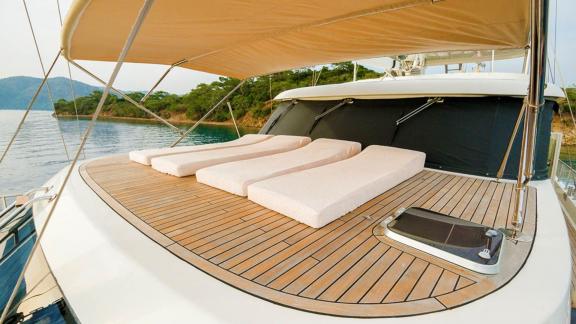 Sun deck of the gulet Vega with three sunbeds under a sunshade, calm water and wooded coast in the background.