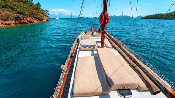 Sun deck of Gulet Lina 2 with cushioned lounging areas, surrounded by turquoise water and green nature.