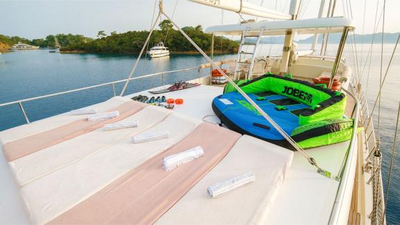 Upper deck of the gulet Vega with sun loungers, towels and water sports equipment, surrounded by calm water and other bo