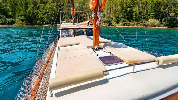 The foredeck of Gulet Lina 2 with sun loungers, anchored in a peaceful bay surrounded by greenery.