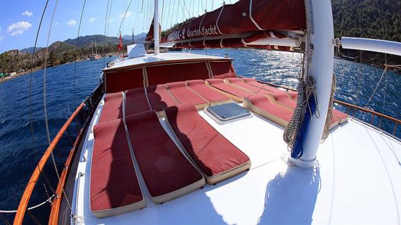 Sonnenliegen auf dem Deck der Gulet Nirvana 2, vor Anker mit bewaldeten Hügeln und Küste im Hintergrund.