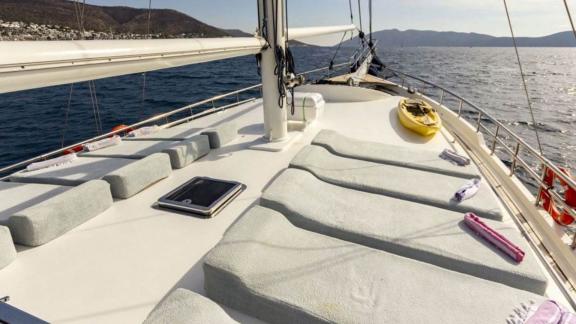 Yelkenli yat The Blue Sea'nin deniz manzaralı güvertesinde güneşlenme alanları ve havlular.