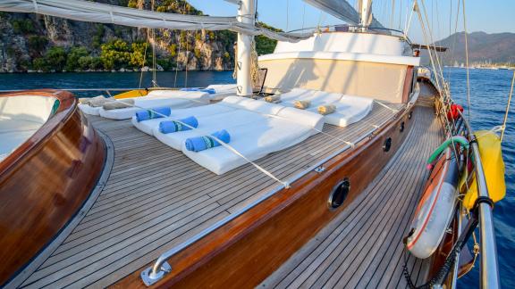 Deck of a luxurious sailing yacht with white sun loungers and towels, anchored in a quiet bay.