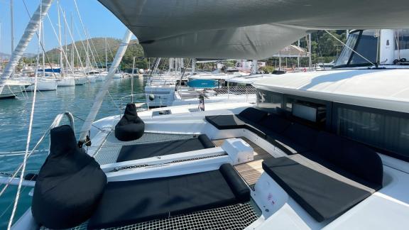 Clara katamaranının ön güvertesindeki rahat dinlenme alanı, liman manzaralı konforlu şezlonglar ve oturma minderleri sun