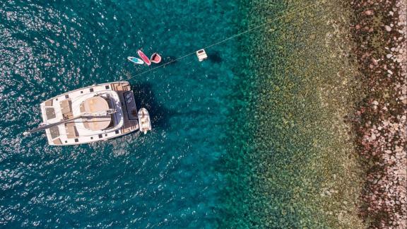 Adara yacht is anchored near the shore in crystal-clear turquoise waters with water toys around.