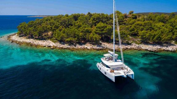 The Sunreef 50 Solitaire catamaran anchors in turquoise waters by a forested island for a peaceful escape.