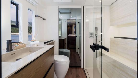 В ванной катамарана Sunreef 50 душ с стеклянными стенками, современная раковина и окно с видом.