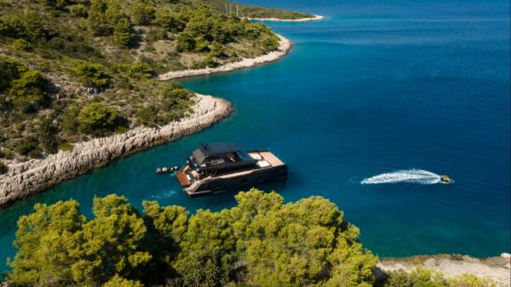 Sunreef 70 catamaran Amber One anchored as jetski glides by in crystal blue waters.