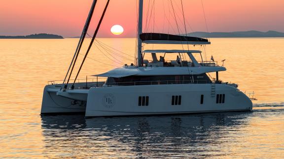 The chartered Honeybird Sunreef 80 sails through golden waters off Šibenik at sunset.