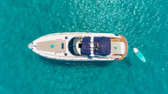 The yacht lies still with a paddleboard floating beside and towels laid out on deck.