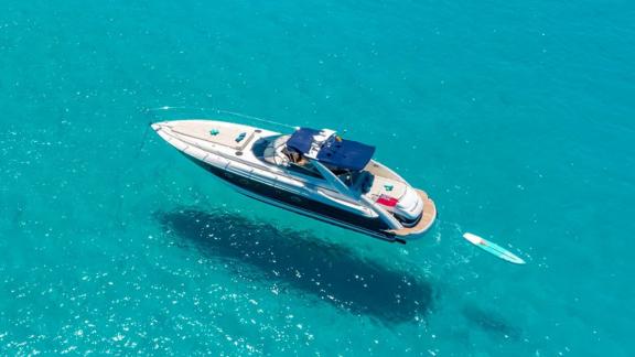 The yacht is anchored in turquoise waters with a paddleboard floating behind.
