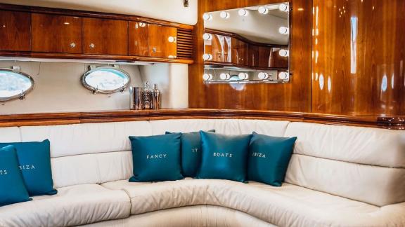 Inside the Fancy It yacht in Ibiza, a cozy cream-colored sofa and round sea-view windows create a relaxing setting.