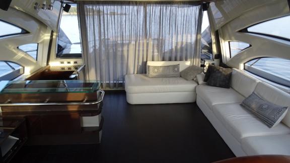 Im Inneren der Yacht Super Toy befindet sich eine gemütliche Sitzecke mit weißen Sofas, umgeben von großen Fenstern.