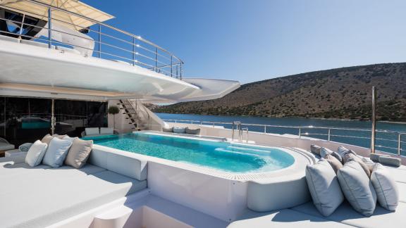 Breathtaking infinity pool on a luxurious yacht, surrounded by white loungers. View of hills and bay.