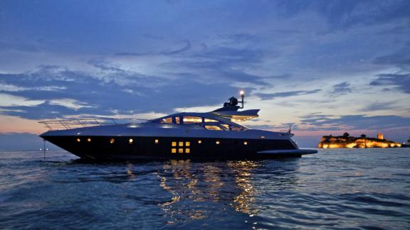 The illuminated motor yacht Thea Malta in front of a picturesque island in Greece. Perfect for nocturnal adventures.