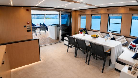 The salon of Beluga 1 in Göcek features a dining table, lounge seating and sea views through large windows.