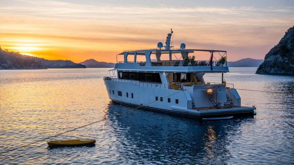 Lila trawler yacht rests calmly at anchor in Fethiye bay under sunset skies.