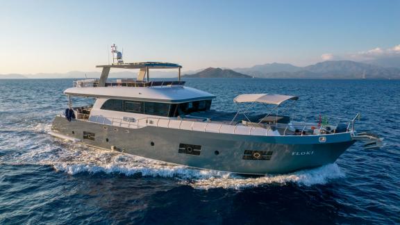 The Floki trawler yacht cruising at sea with mountain scenery in the background.