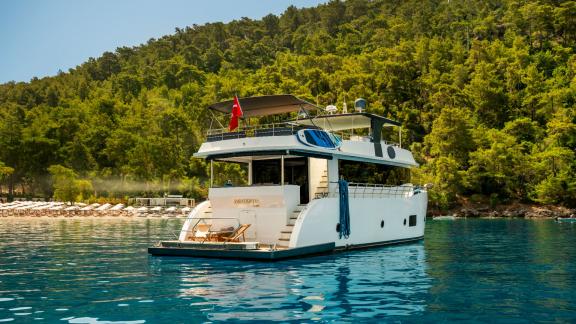 The yacht Oggusto is anchored peacefully near pine forests with sunbeds at the stern in Fethiye.