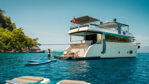 A woman enjoys paddleboarding behind the anchored Oggusto trawler in scenic Fethiye waters.