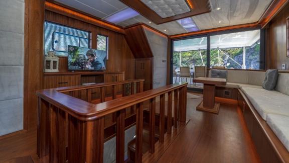 Lounge area with TV and polished wooden staircase leading to the lower deck aboard the Oggusto yacht.