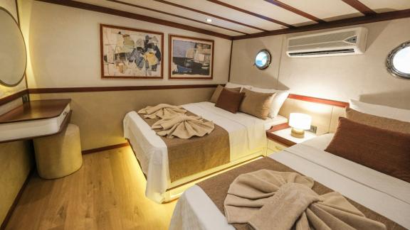 The double cabin of the Gulet Tarkan in Turkey with two large beds, decorative towels, stylish wall paintings