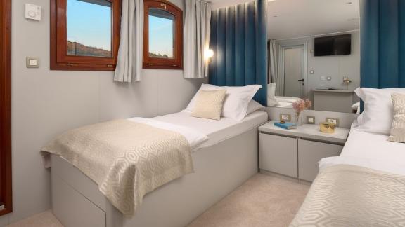 Bright twin-bed cabin on the Bellezza yacht with cozy beds and windows offering sea views.