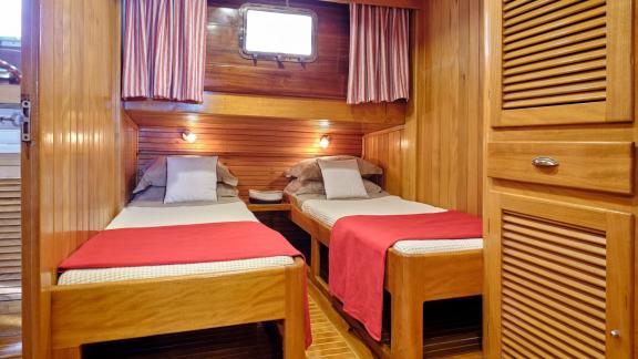 The wooden twin cabin of White Pearl gulet in Athens includes two single beds and storage units.