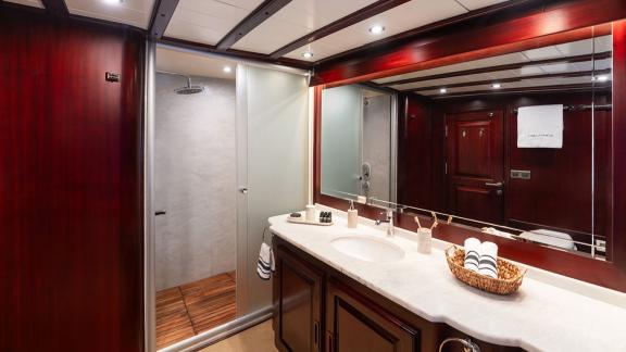 In Göcek gulet charter option Always Smile bathroom with shower area sink mirror and storage cabinets clearly visible.