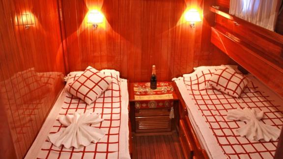 A cabin on Gulet Il Fratello with two single beds, wooden furniture, warm lighting, and a bottle of champagne on the nig